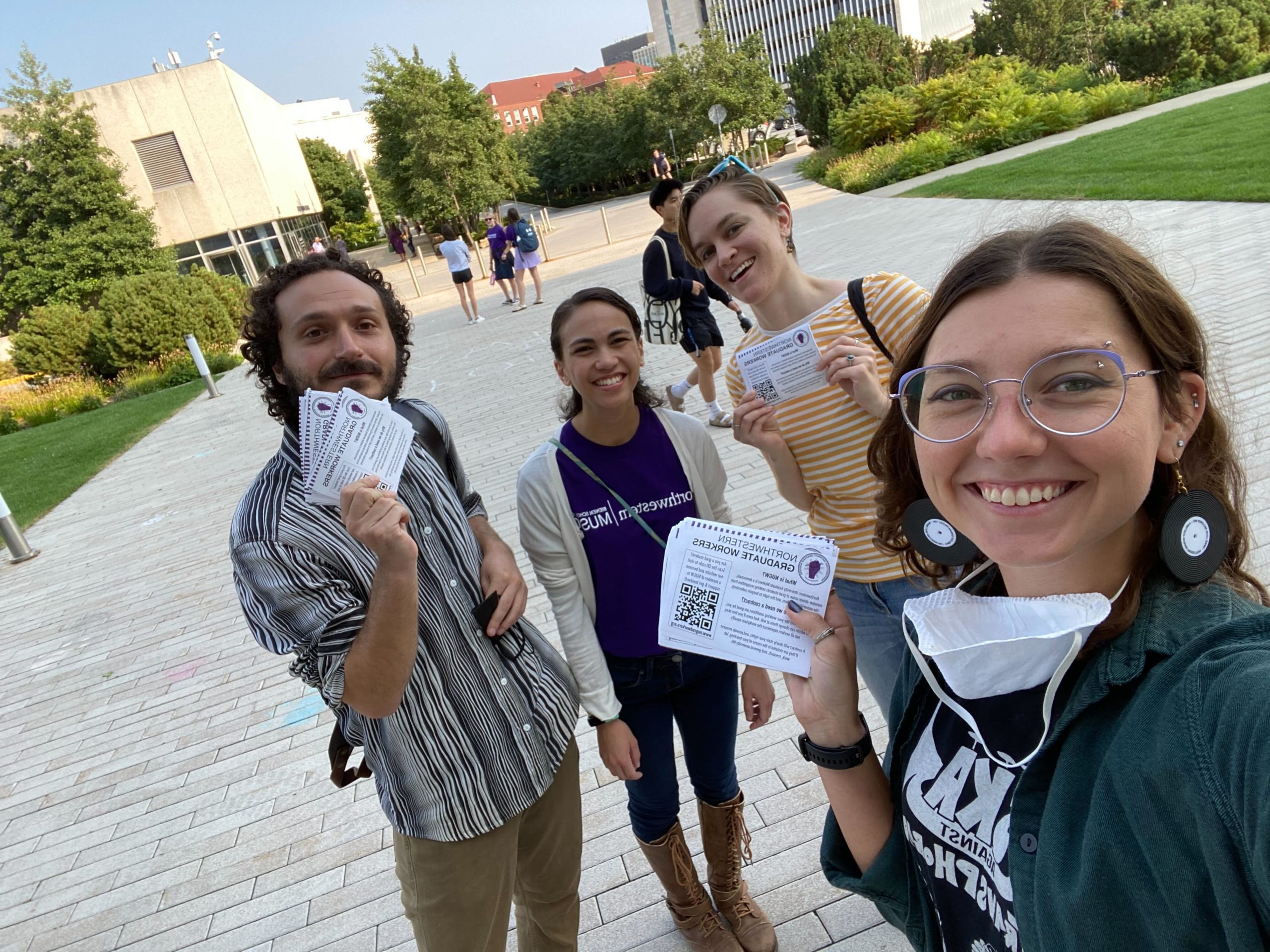 four nugw members smiling and holding up flyers they are passing out